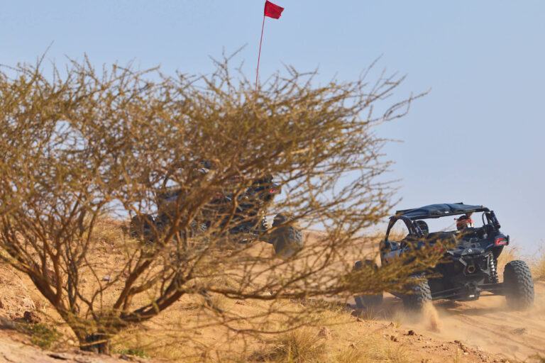 Can-Am X3 buggy riding past desert trees at Al Badayer