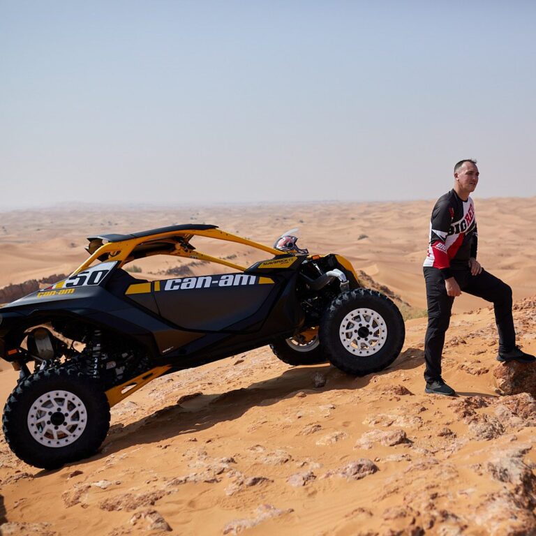 Big Red guide beside a Can-Am Maverick R 2-seater buggy on a desert ridge near Dubai